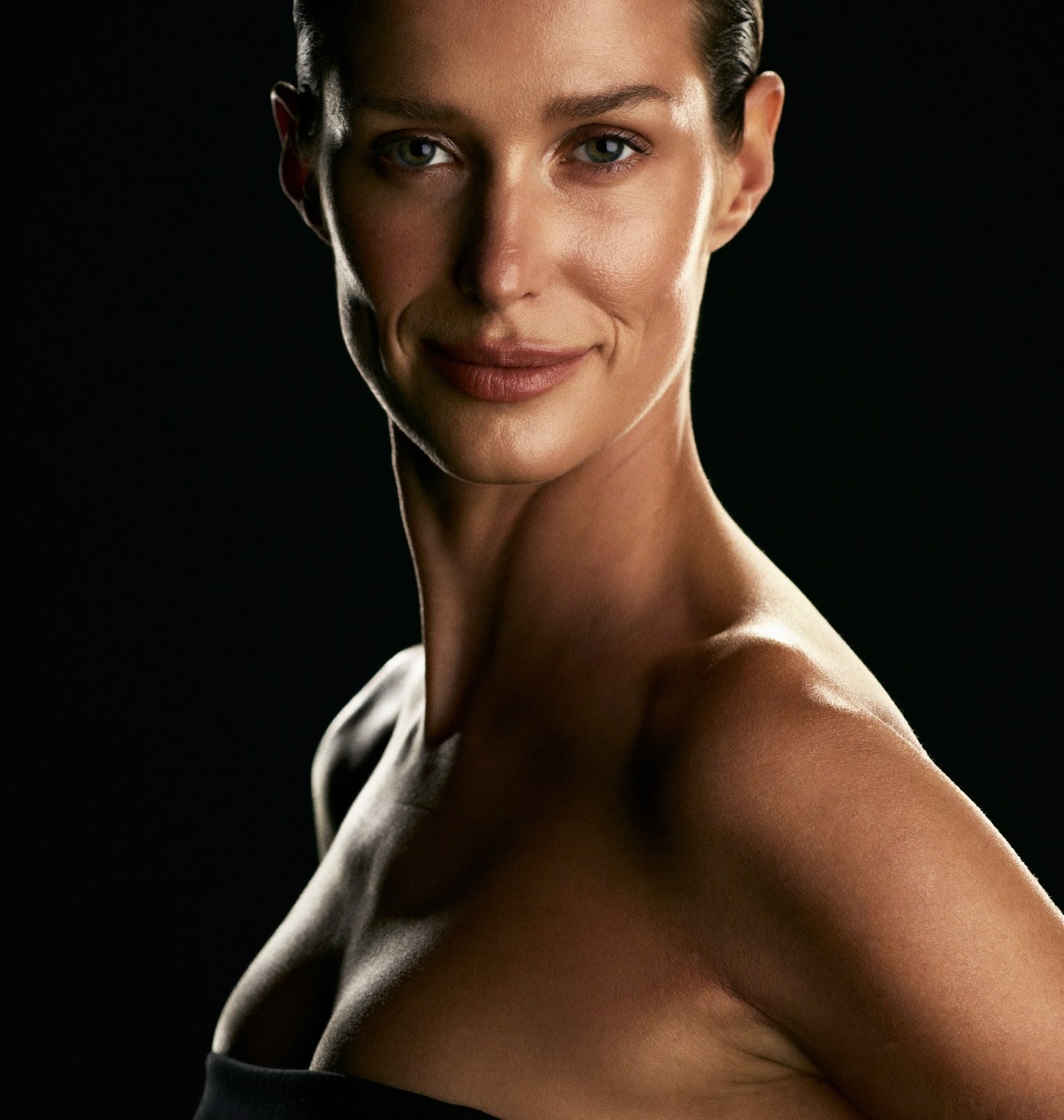A confident woman in her early fifties with natural, refined, well-rested features, lit against a dark background